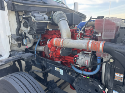 Kenworth T680 engine bay showing red-orange engine block, intake pipe, hoses, and surrounding components.