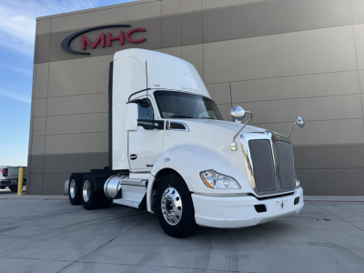 Kenworth T680 tractor in front of a building with MHC logo; white cab, large grille, sleeper, dual rear axles visible.