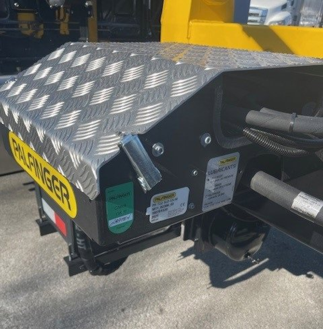Front-left view of a new 2026 Hino L7 hooklift truck showing diamond plate step, lubricant label, and hydraulic components with warning stickers.