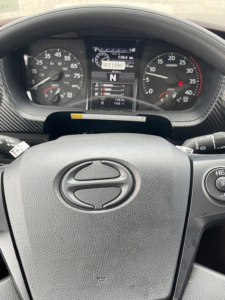 Dashboard view of a 2026 Hino L7 steering wheel with instrument cluster and digital display in center showing N gear; visible speedometer and tachometer on either side.
