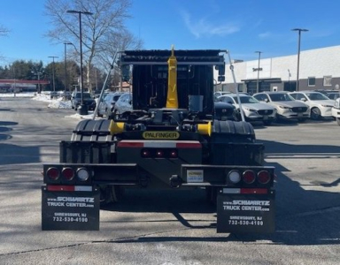 Rear view of a new 2026 Hino L7 hooklift truck on a lot, with yellow lifting hook and hitch system, taillights, and Schwarz Truck Center mud flaps visible.