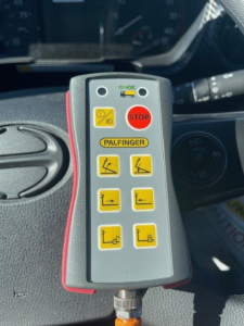 Control pendant showing yellow safety icons and a red STOP button inside a Hino L7 truck cab.