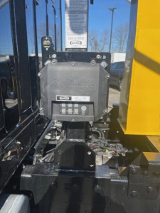 Hooklift truck cab interior showing control panel with buttons and labels mounted on a black chassis near a yellow body, VIN tag visible in background.