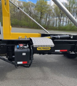 Hino L7 hooklift truck side with Palfinger hydraulic system and yellow frame showing exterior components and decals.