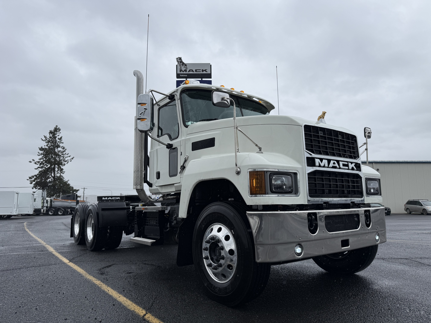 Mack PI64T conventional daycab truck showing front grille with Mack emblem and large bumper, white cab, dual rear axles, side exhaust stacks, and chrome wheels.