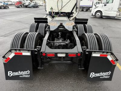 Mack PI64T tractor rear view showing dual rear axles, fifth wheel mount, mudflaps with Bruckner's Equipment logo, and trailer brake lines in a truck lot.