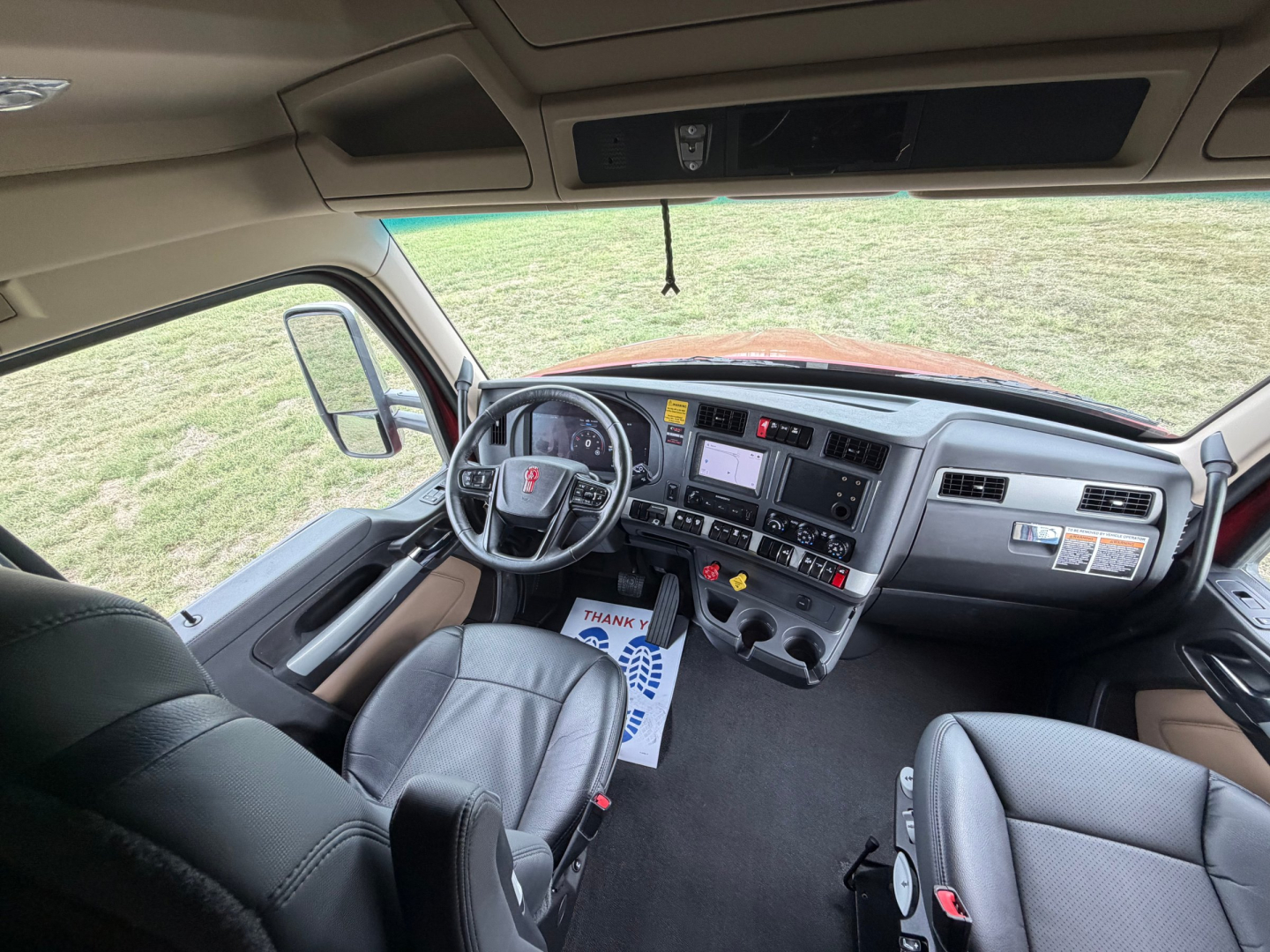 Kenworth T680 cab interior with steering wheel, dashboard, and front seats visible; large touchscreen and control panel on center console; beige and black interior trim.