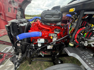 Kenworth T680 engine bay with red engine and blue intercooler hoses, BX15 badge visible, multiple black hoses and electrical cables in the dash area.