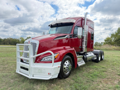 Kenworth T680 tractor in red with large chrome grille guard and dual rear axles, side view showing sleeper cab and chrome fuel tanks.