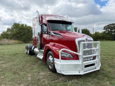 Kenworth T680 conventional sleeper truck with chrome bumper guard, red cab, large grille, side mirrors, and dual rear wheels on a grassy field.