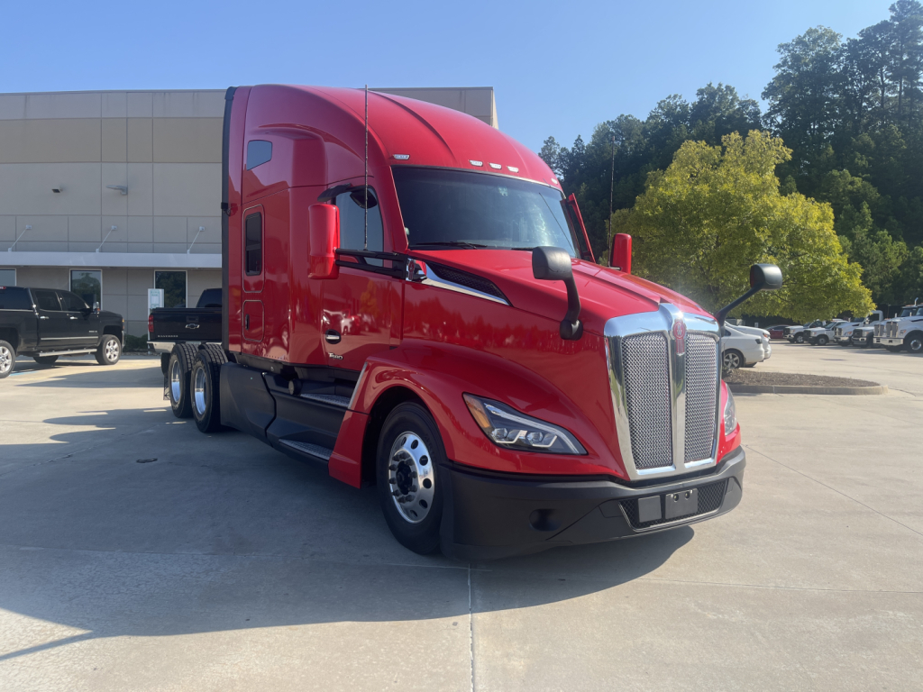 Kenworth T680 tractor in red, front-left view, with sleeper cab, chrome grille, and black bumper. Details show truck exterior, headlights, mirrors.