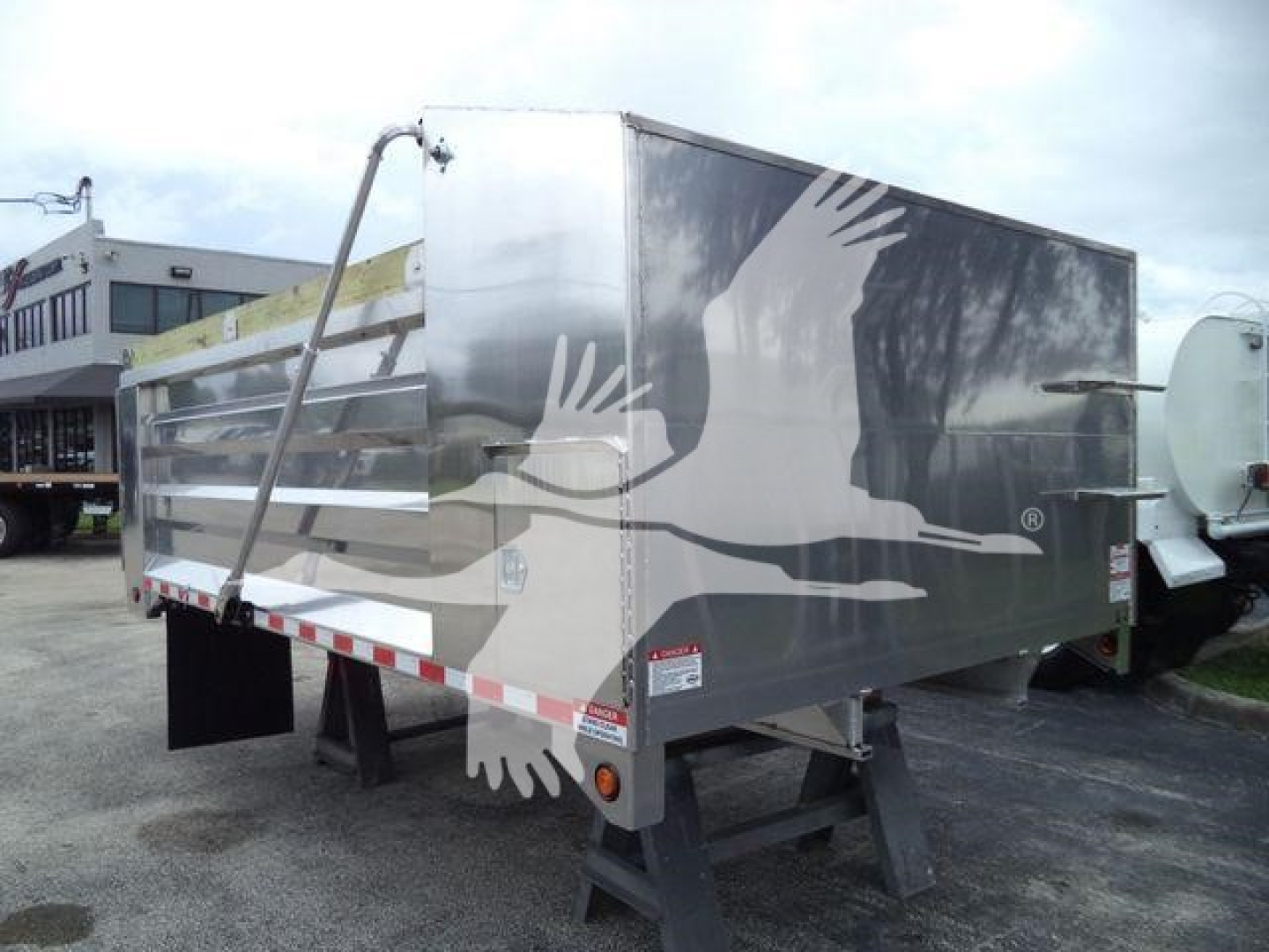 Dump truck trailer with aluminum side panels showing an industrial logo of birds in flight; rear view with support legs.