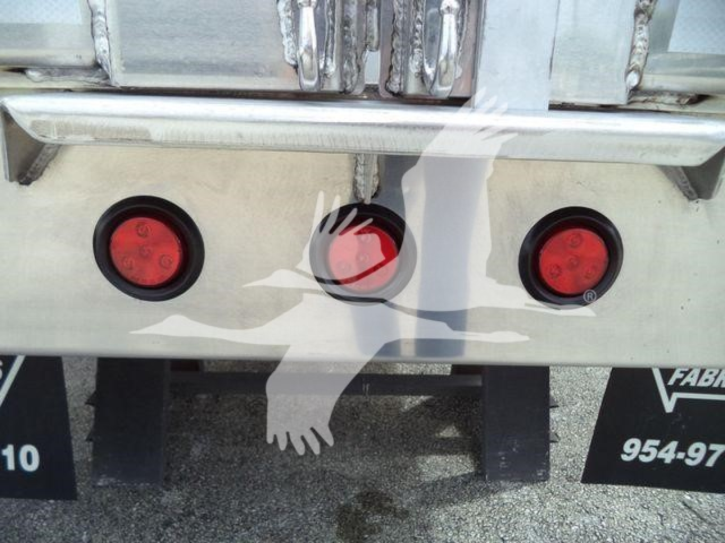 Back of dump trailer showing three circular taillights and a central circular reflector; chrome bumper and decorative eagle graphic on aluminum surface.