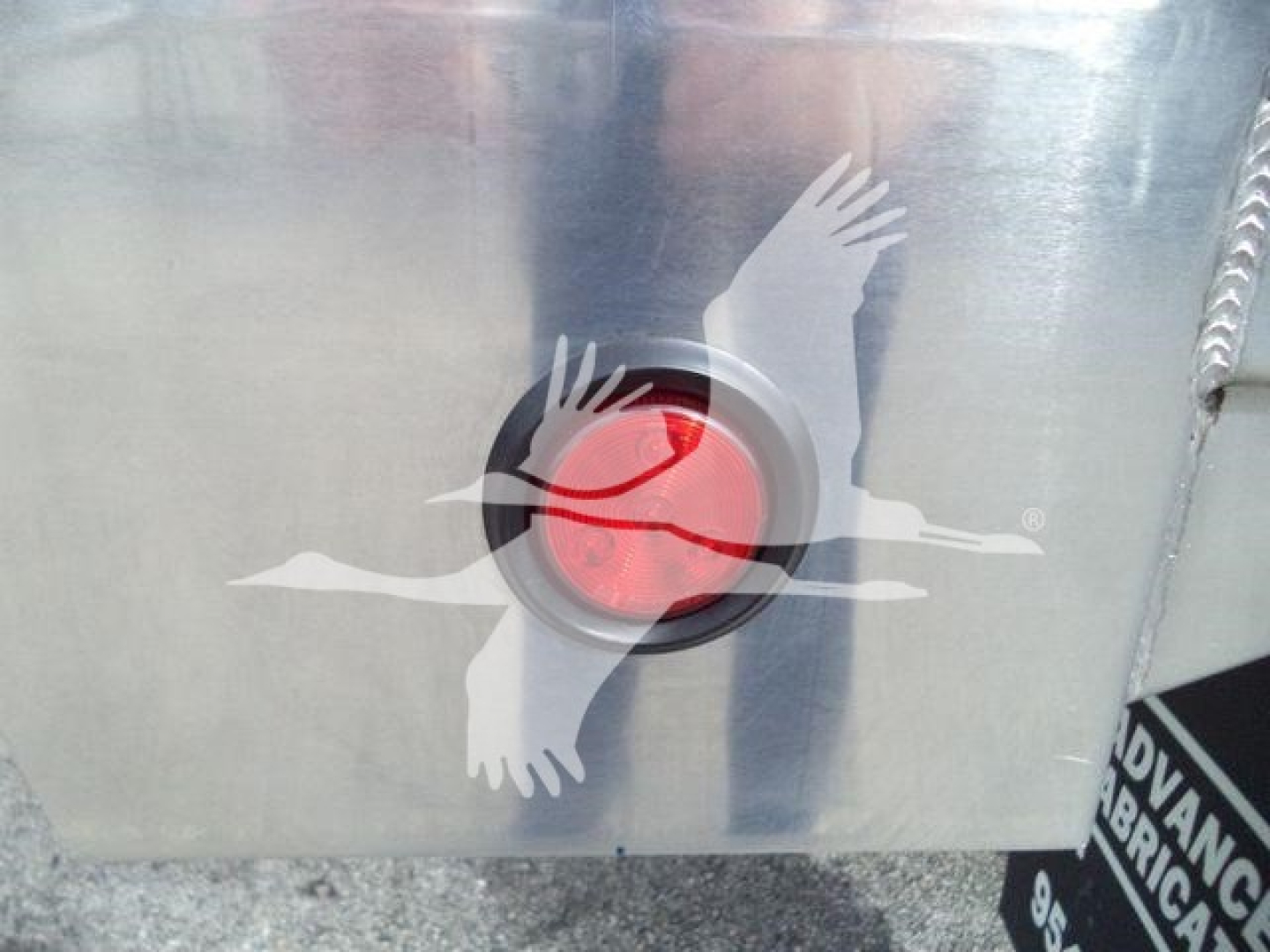 Aluminum dump trailer side showing a red circular reflector with a white gull logo and a welded seam.