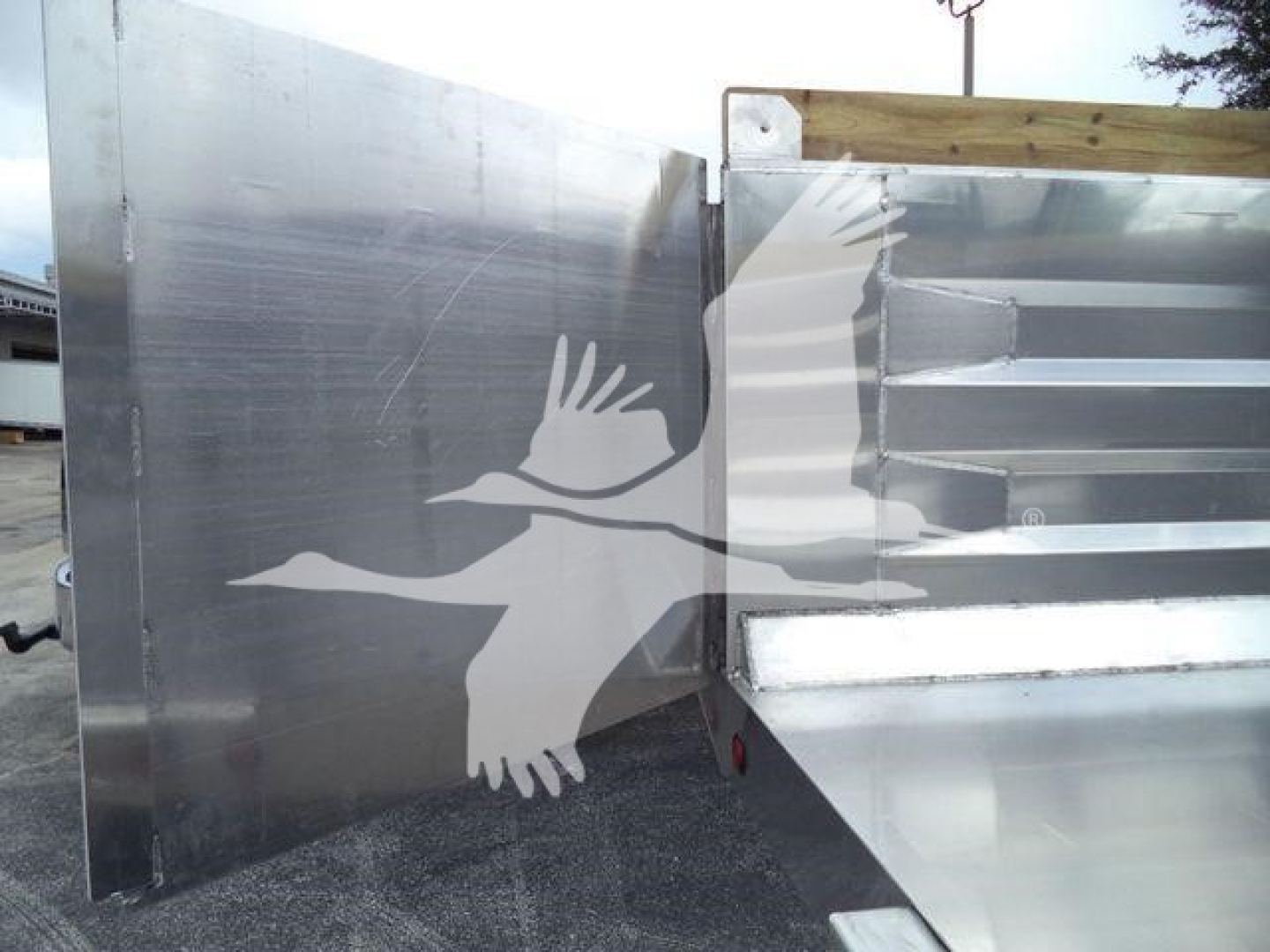 Dump truck bed with aluminum side panel and rear gate showing reflective metal surface and a white bird graphic on the side.