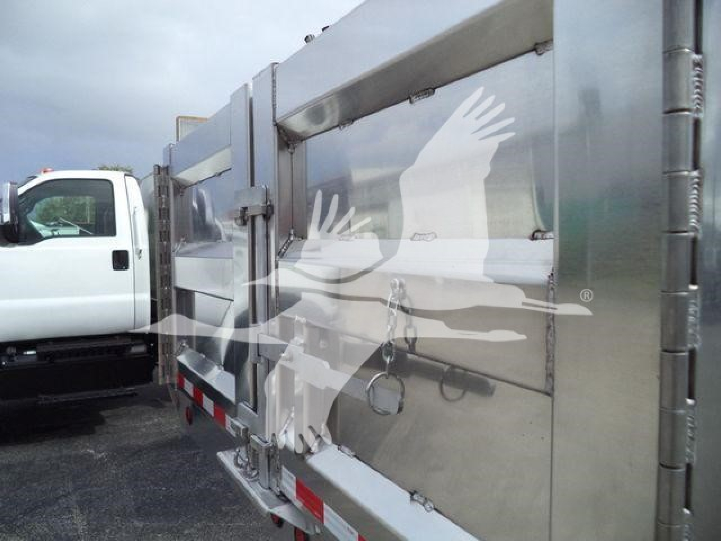 Dump truck bed side with metallic panels and latch handles; logo watermark visible; aluminum trailer with side panel details.