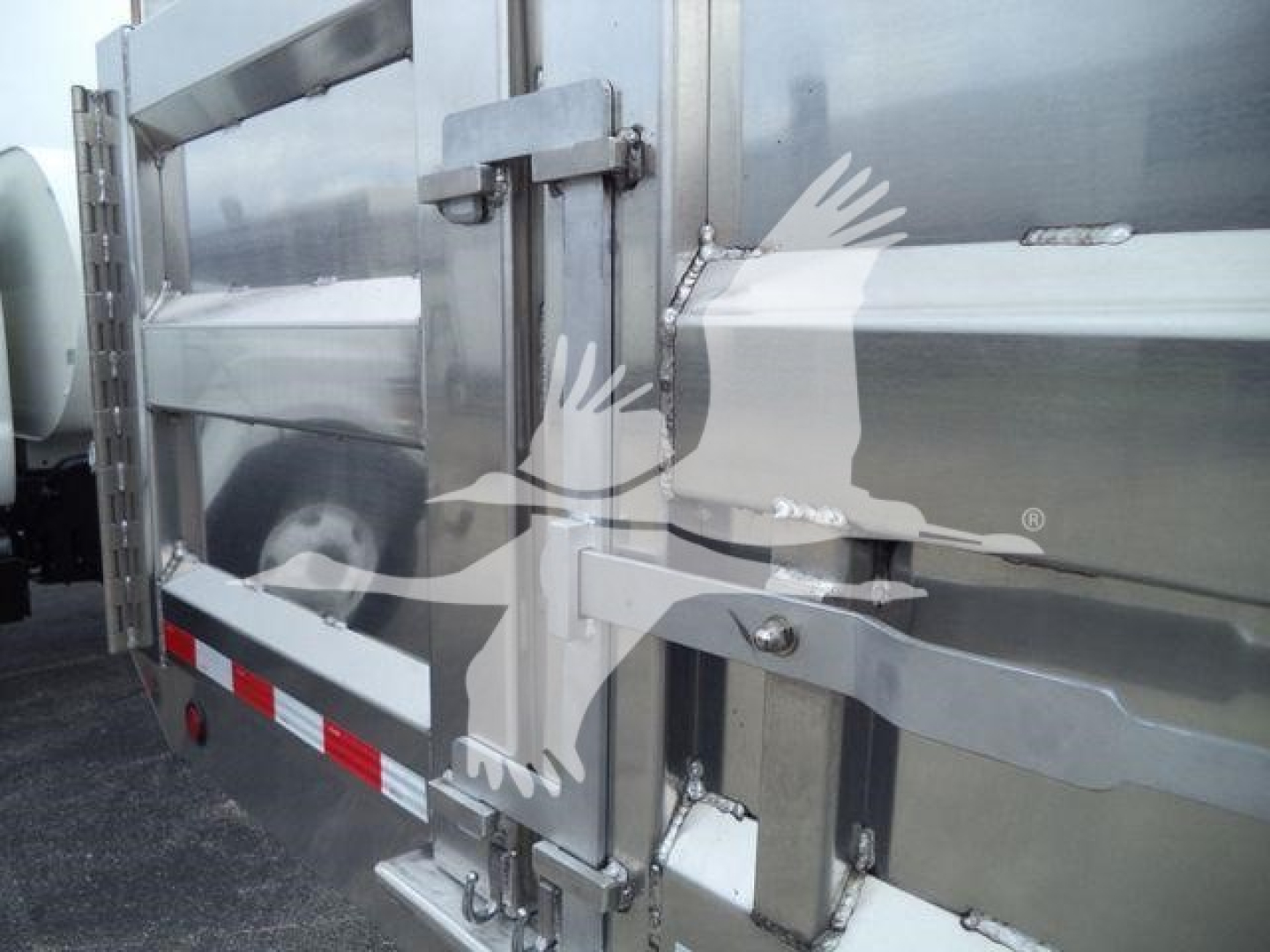 Dump truck body with rear metal doors and latches visible; branding graphic overlaid from watermark.