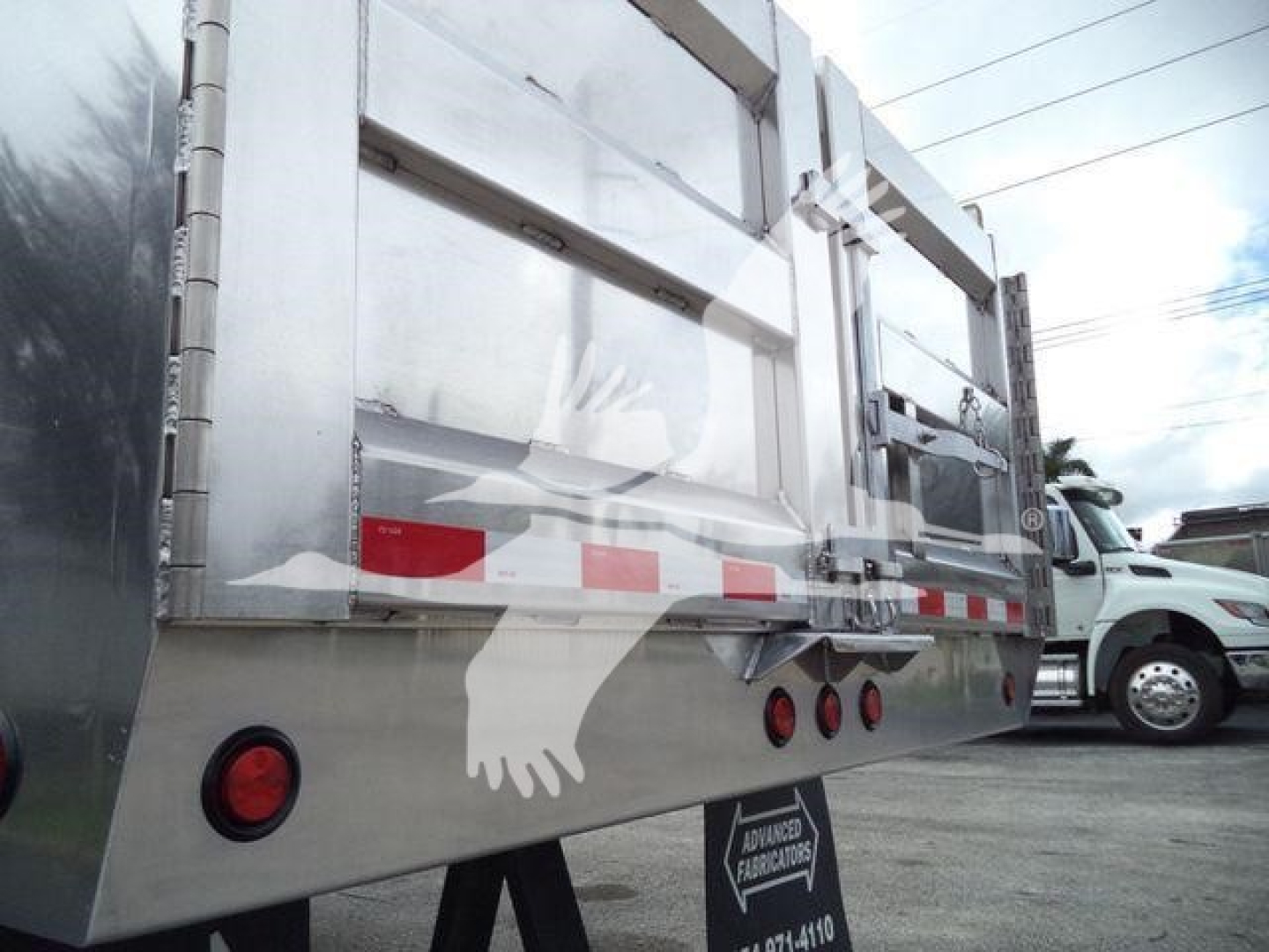 Dump truck bed side view showing metal alloy panels, rear reflectors, and stock number tag on a 2025 Advanced Fabricators 14 ft aluminum dump body.