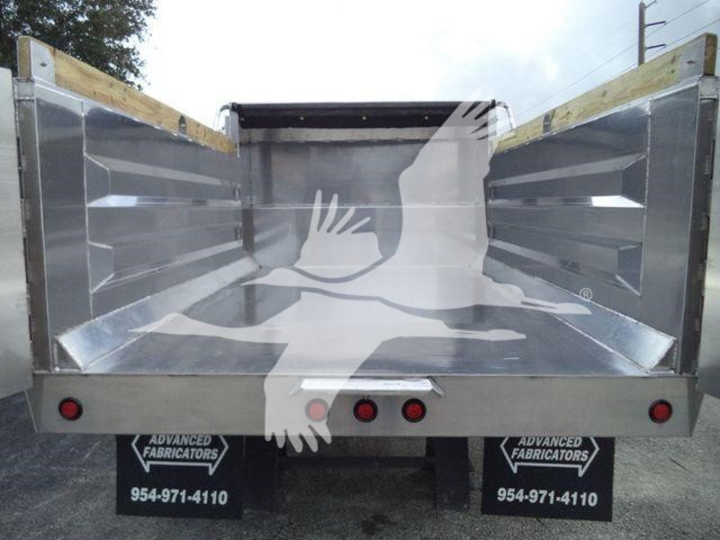 Dump truck bed of a 2025 Advanced Fabricators 14 ft aluminum dump trailer showing aluminum side walls and tailgate with two red taillights and branding signs reading Advanced Fabricators 954-971-4110.