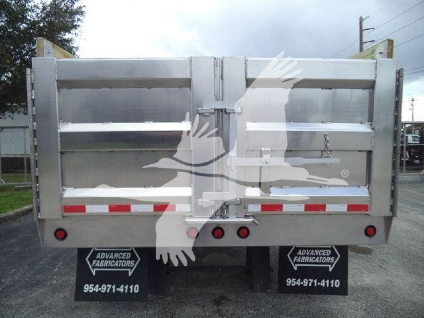 Dump truck bed rear showing metal tailgate with latch and dual red rear lights; mudflaps display Advanced Fabricators branding and contact number.
