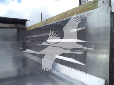 Truck dump bed side with metal panels and a logo showing three white birds overlapping.