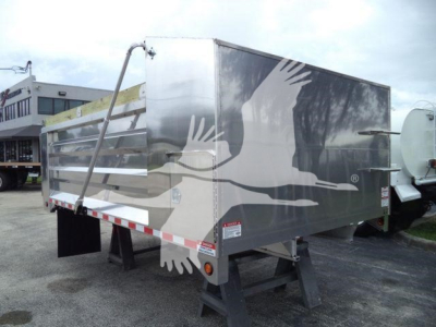 Dump truck trailer with aluminum side panels showing an industrial logo of birds in flight; rear view with support legs.