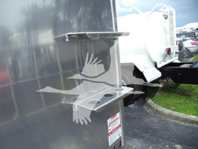 Trailer side with aluminum dump body showing mounting bracket and step plate; small safety sticker visible on lower panel.