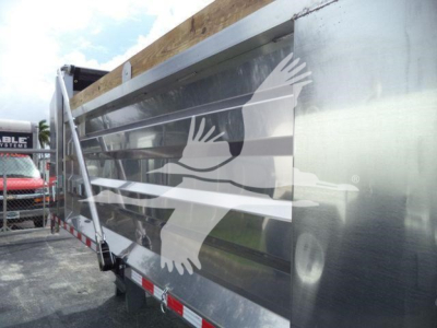 Dump truck trailer side with aluminum surface and large reflective logo depicting birds in flight, 14 ft layout.