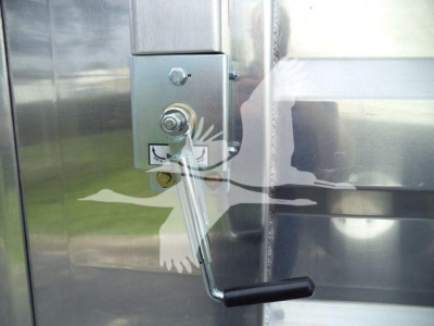 Metal dump trailer hitch hand crank and latch on polished aluminum side panel showing handle in foreground