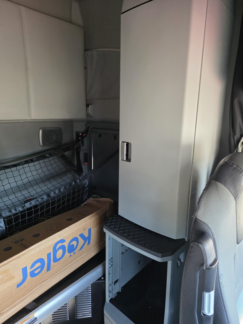 Truck cab interior showing storage cabinet and step, with Kenworth box and wiring netting visible.