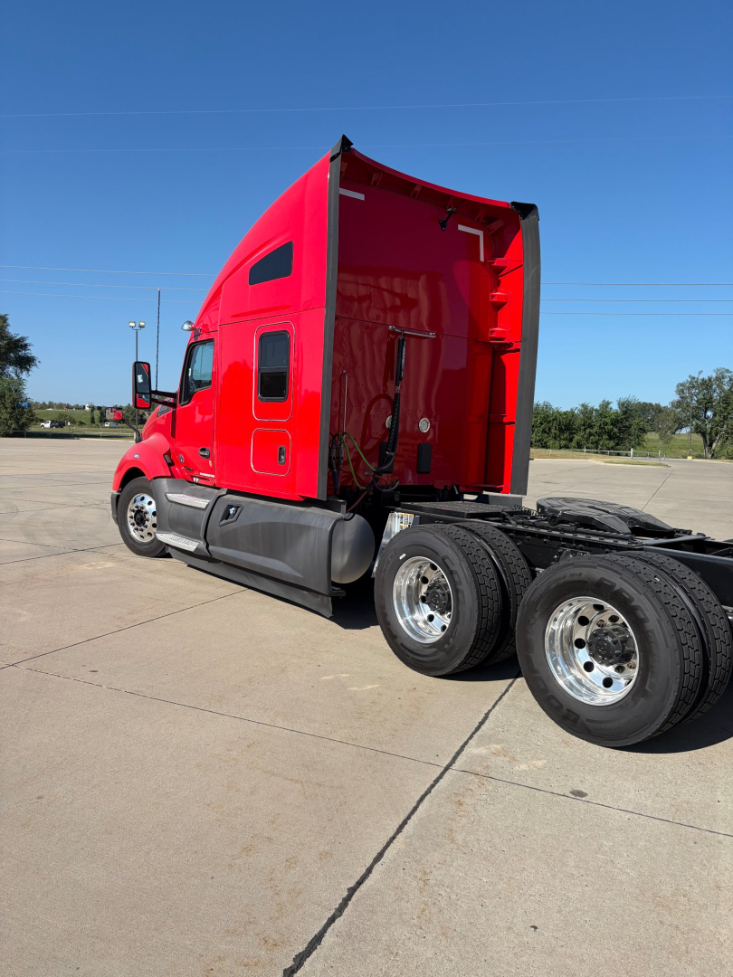 Kenworth T680 tractor cab in red with raised sleeper, side view showing rear wheels and chassis; exterior features visible.