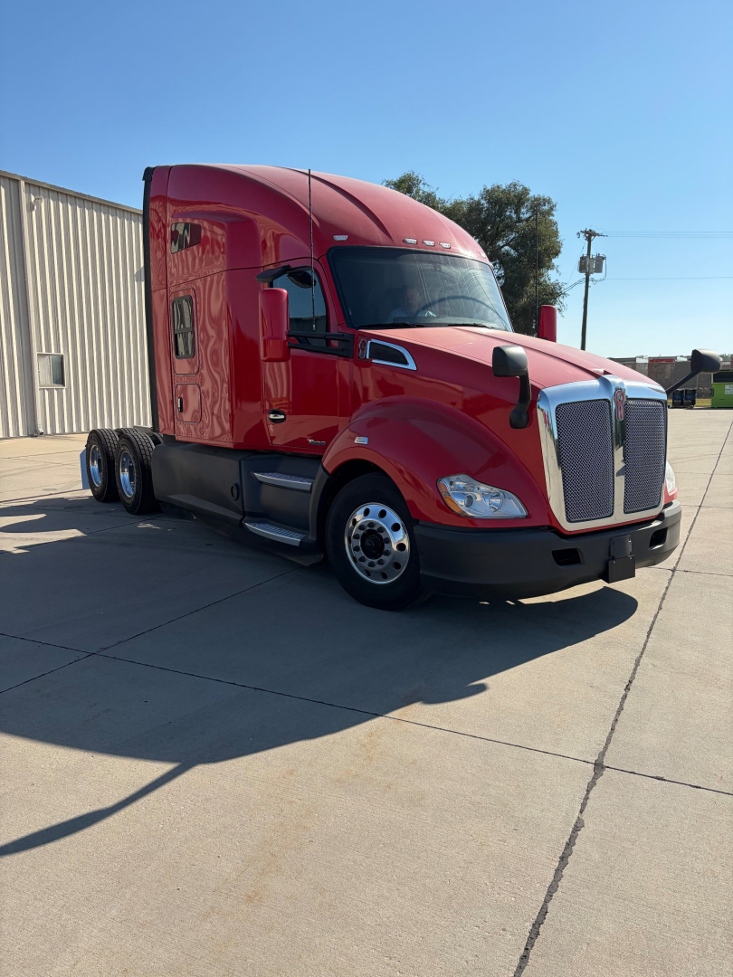 Kenworth T680 semi-truck with red cab, front grille, two side mirrors, sleeper cabin, on a concrete lot.