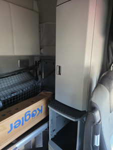 Truck cab interior showing storage cabinet and step, with Kenworth box and wiring netting visible.