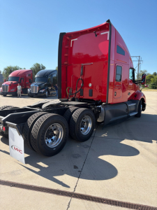 Kenworth T680 sleeper cab truck rear three-quarter view showing dual rear axles and red paint; no visible text legible on the truck body.