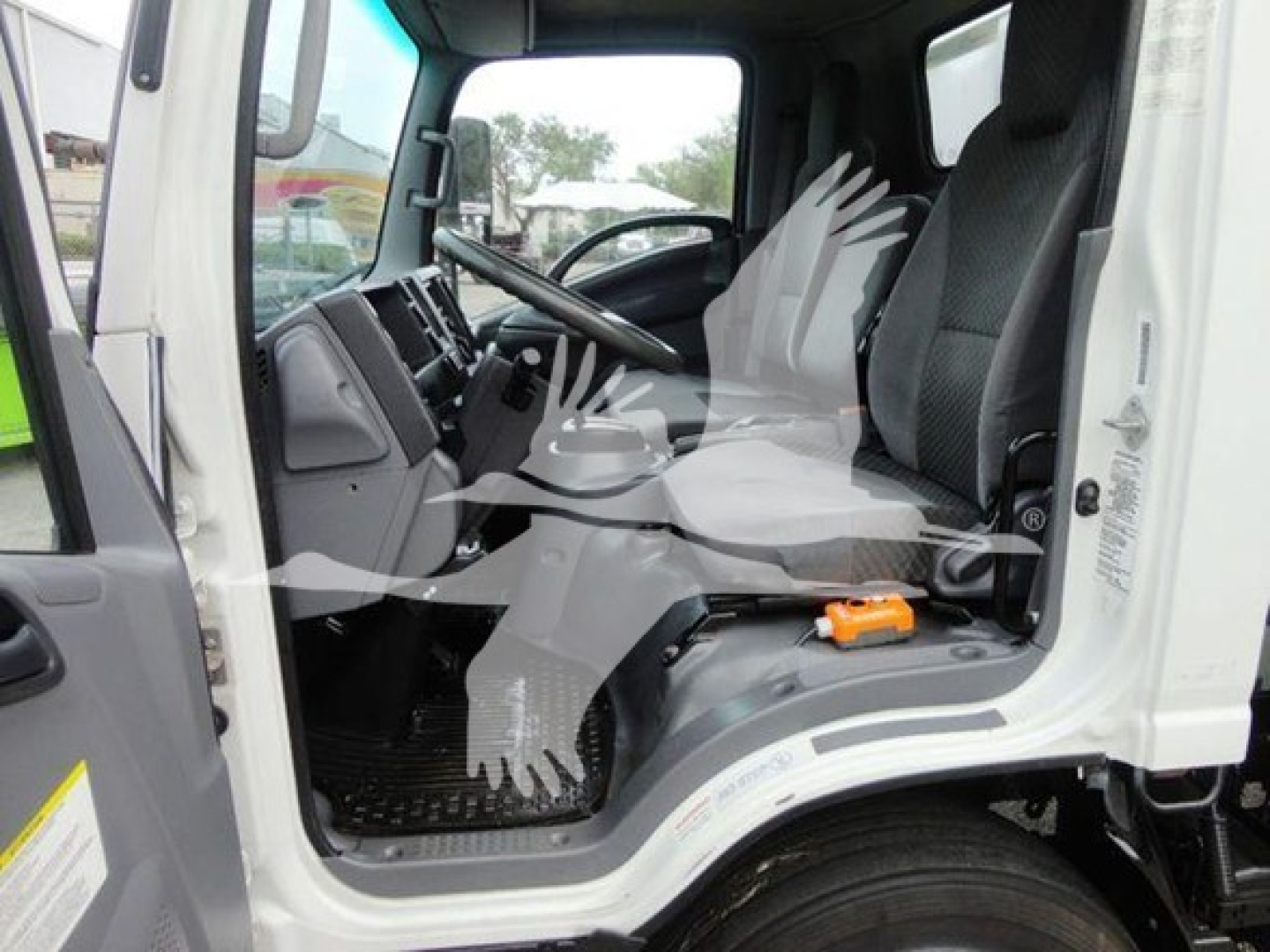 Isuzu NQR cab interior view showing steering wheel, dashboard, driver seat, and entry step; white exterior and black floor mat visible.