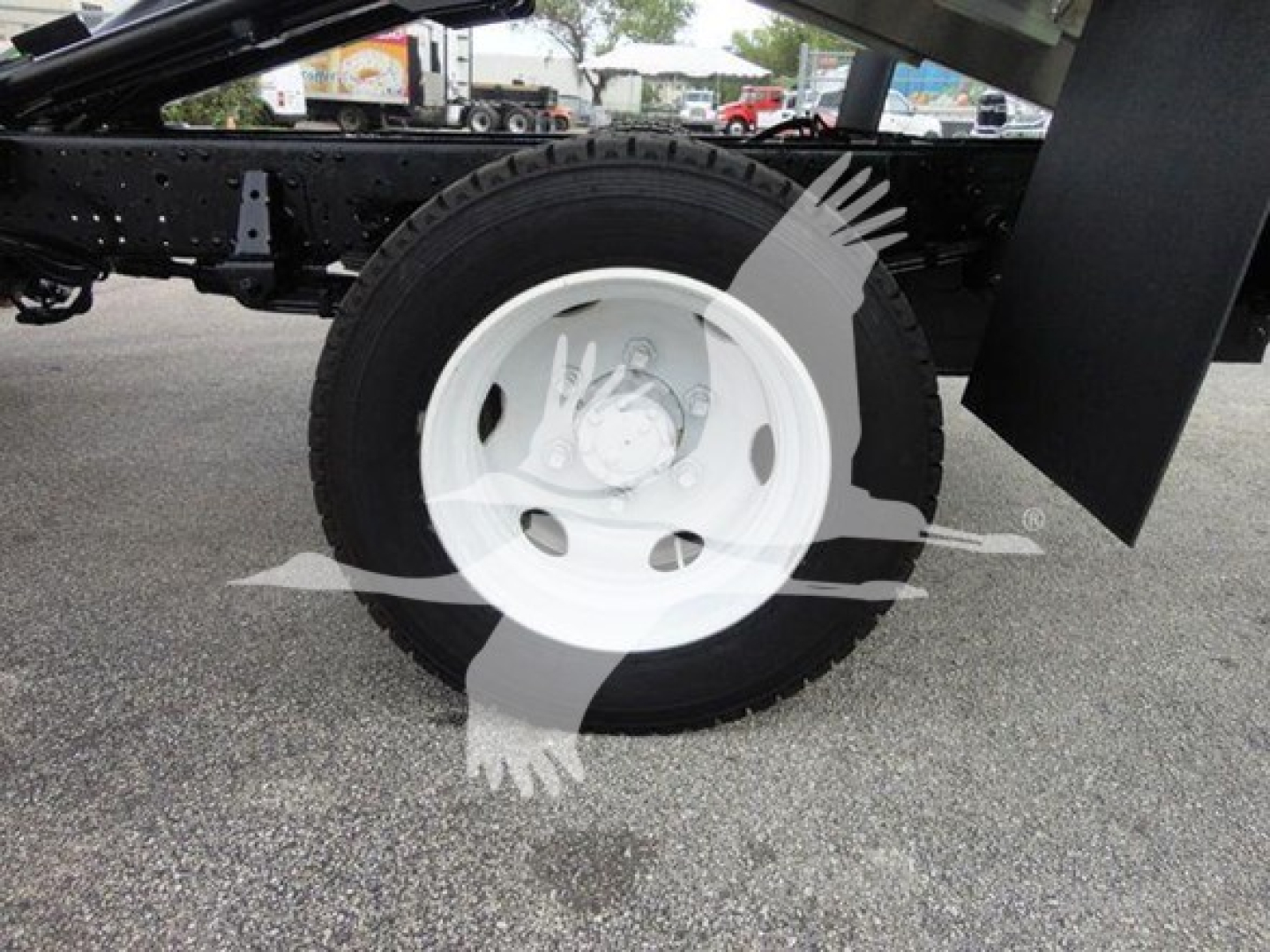Isuzu dump truck chassis showing front wheel and tire; white steel wheel; part of chassis and mud flap visible.