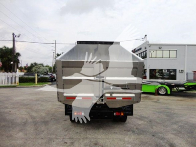 Isuzu NQR dump truck viewed from the rear, with a silver dump bed and black chassis on a paved lot; white and red reflective markings on the rear; a building and another green vehicle in the background.