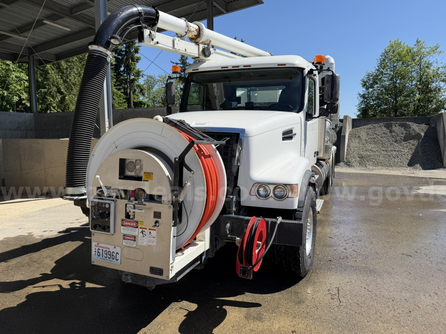 Volvo VHD vacuum truck showing a hose reel and front grille with warning labels.
