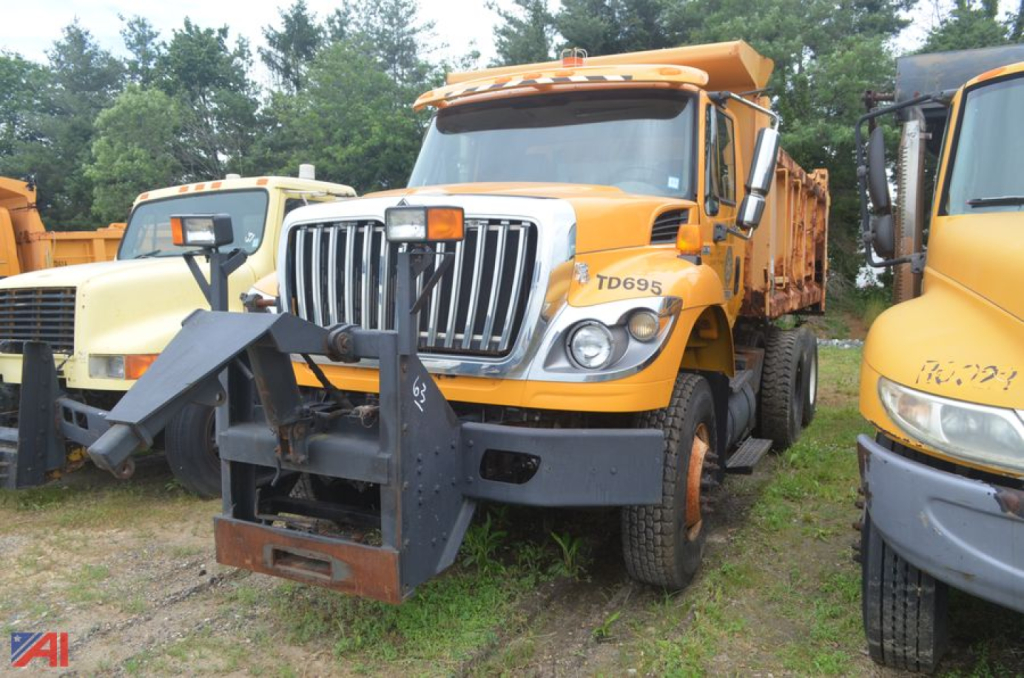 Dump truck front view showing chrome grille, TD695 badge, and snow plow mount on a yellow International WorkStar 7400 with open bed in a lot.