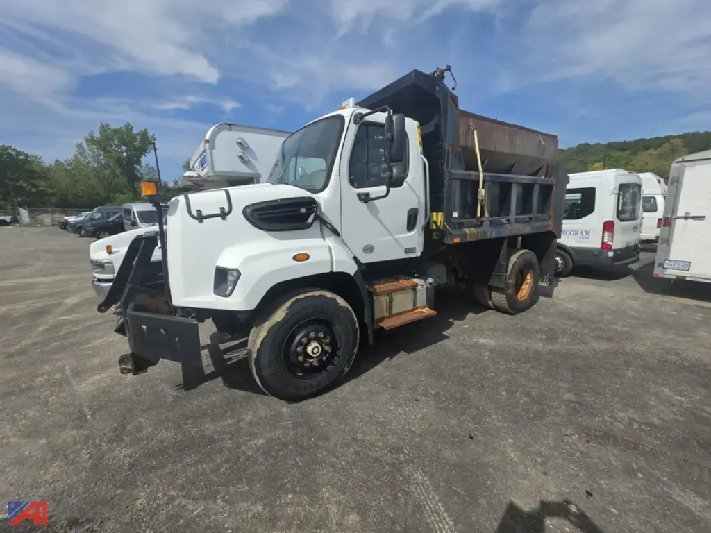 Dump truck with dumping bed, white Freightliner 108SD, front view showing cab and side of bed, indicating VIN 1FVAG5BS9DHFA4388 in a used truck lot.
