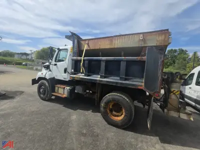 Dump truck side view showing open-top dump bed, white cab, black underbody, and rusted rear wheels on a Freightliner 108SD.