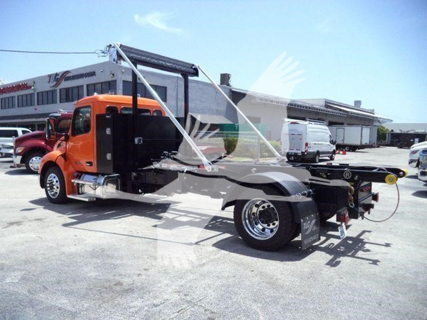 Peterbilt 536 cab-forward chassis in orange, side view, with open cargo area and wheel-lift assembly, in a dealership lot.
