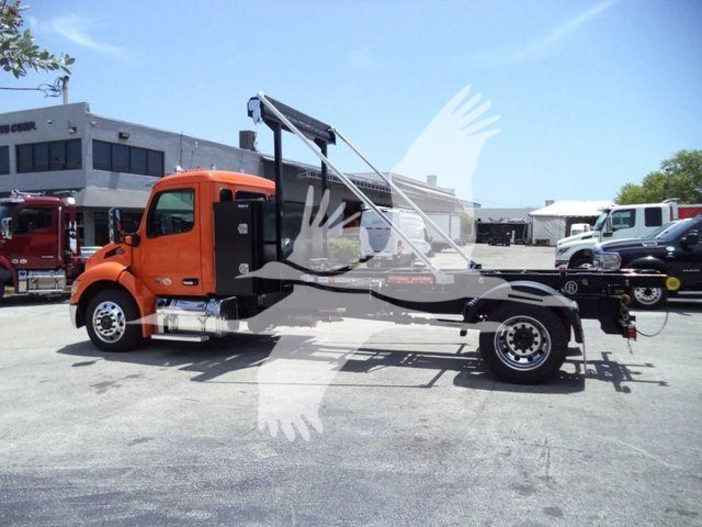Peterbilt 536 chassis with crane/hoist in orange cab and black/truss frame, side view, with dealership lot in background.
