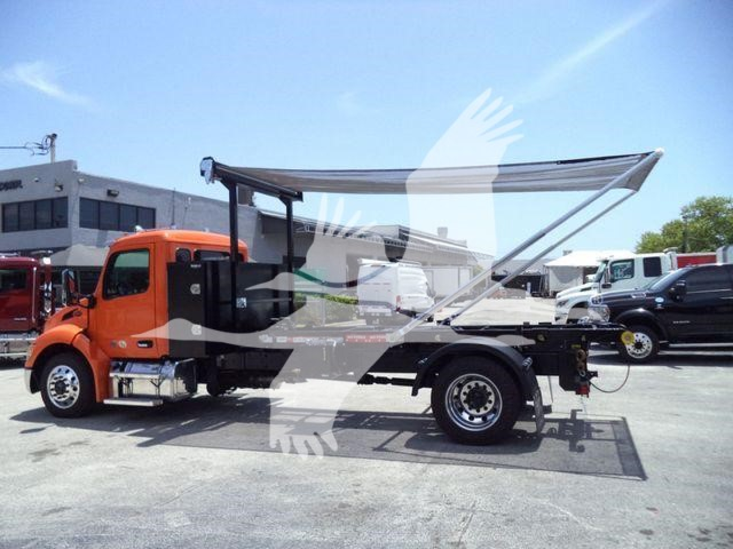 Peterbilt 536 truck in a lot with a raised bed canopy and open rear storage; orange cab, black chassis, white trucks in background.