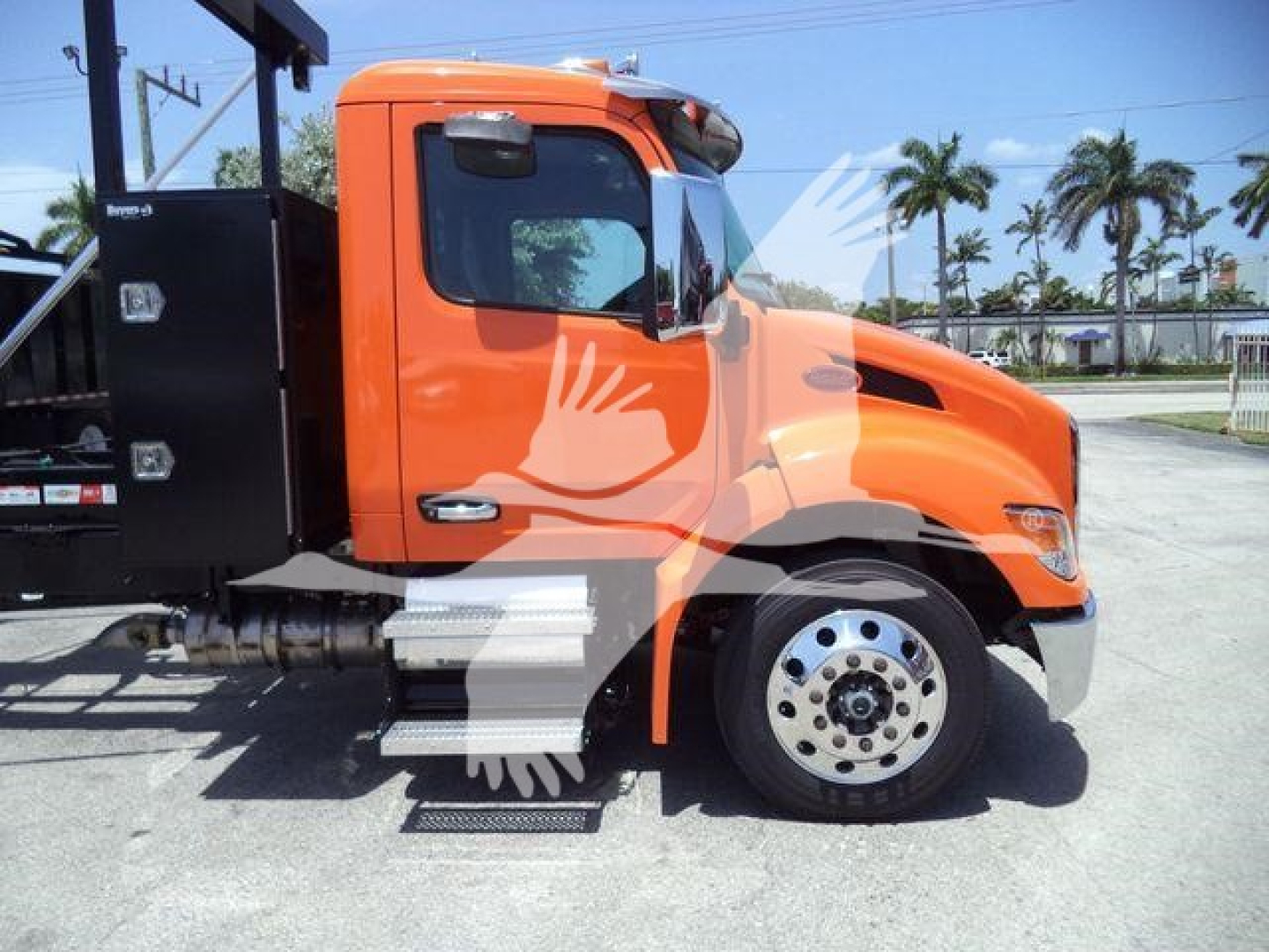 Peterbilt 536 side cab view showing bright orange exterior and front wheel with chrome hub, step, and black utility box in background.