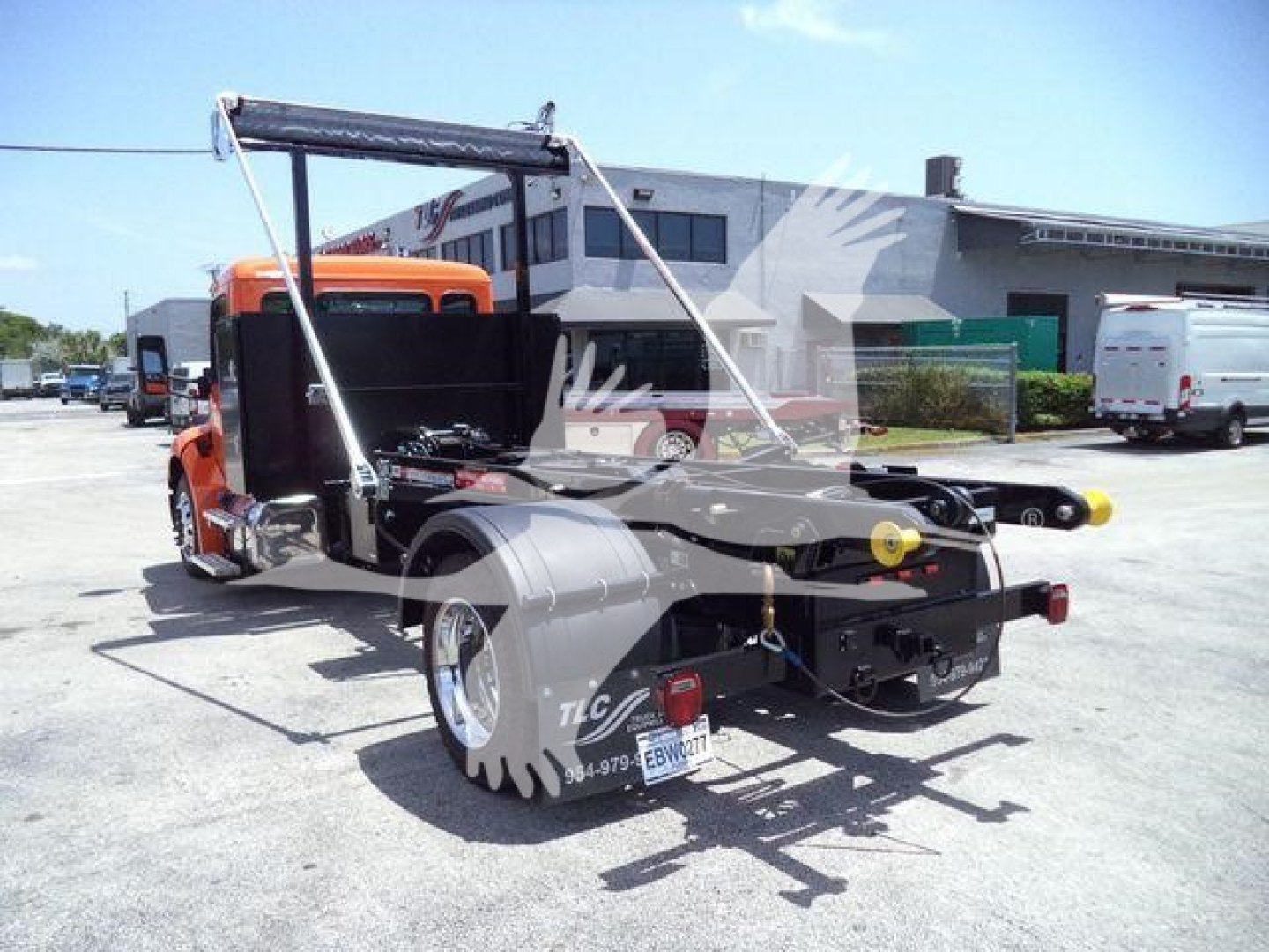 Peterbilt truck chassis with extended rear bed for wrecker setup, orange cab, rear view shows twin wheel dual rear axle, tow apparatus and license plate area.