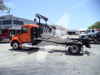Peterbilt 536 chassis with crane/hoist in orange cab and black/truss frame, side view, with dealership lot in background.