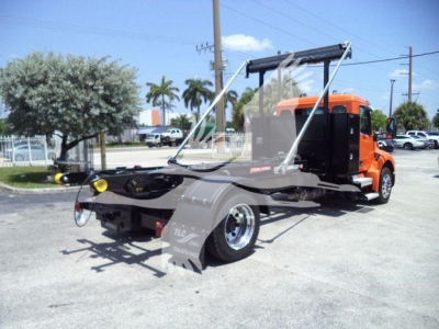 Peterbilt 536 tow truck chassis view with orange cab and flatbed loader, front quarter view showing windshield, chrome wheels, and rear hoist apparatus.