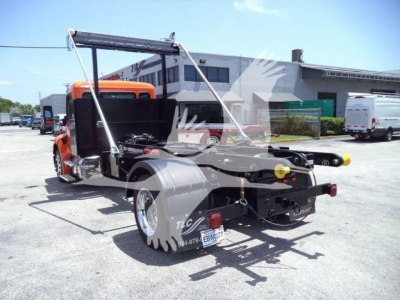 Peterbilt truck chassis with extended rear bed for wrecker setup, orange cab, rear view shows twin wheel dual rear axle, tow apparatus and license plate area.