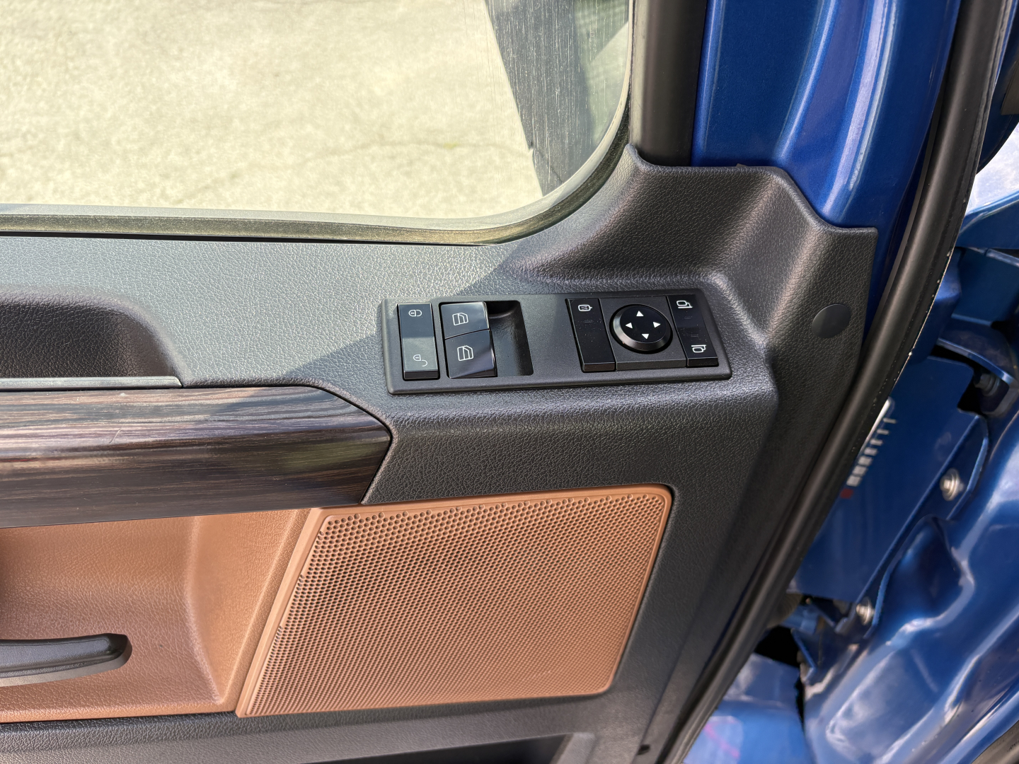 Cab interior of a Freightliner Cascadia 126 showing the door panel with wood trim, speaker grille, window controls, and mirror control dial.